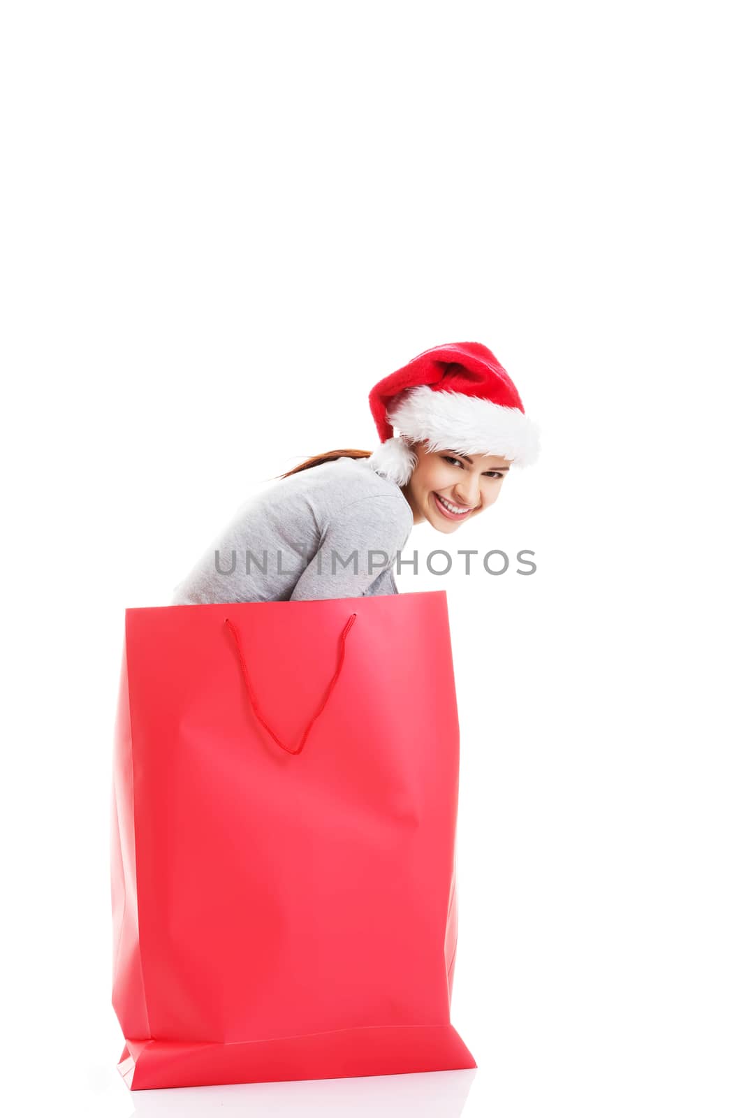 Beautiful girl wearing santa hat in red shopping bag. Isolated on white.