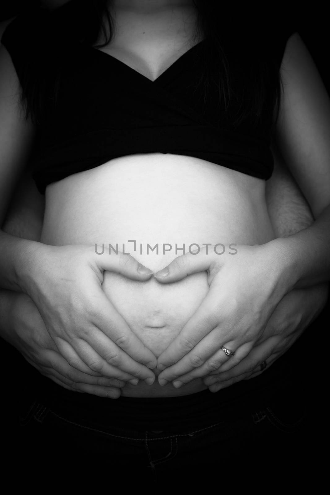 Pregnant woman making heart shape with hands over her stomach  by Izaphoto