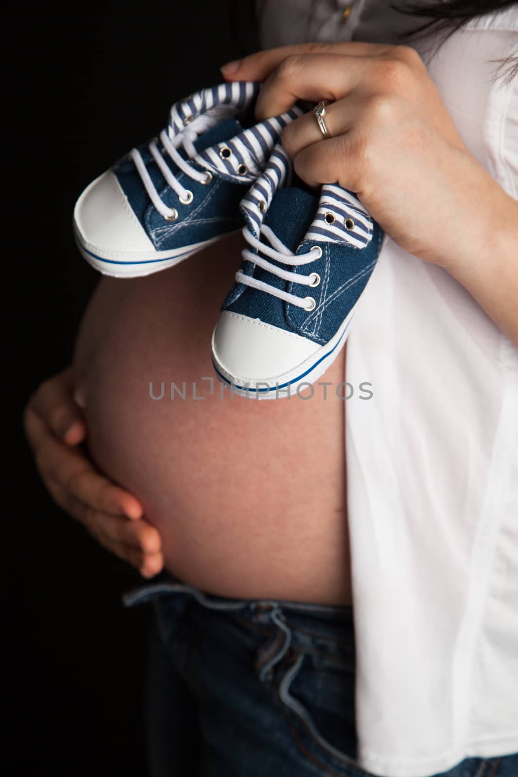 Pregnant woman holding a pair of baby shoes on her belly by Izaphoto
