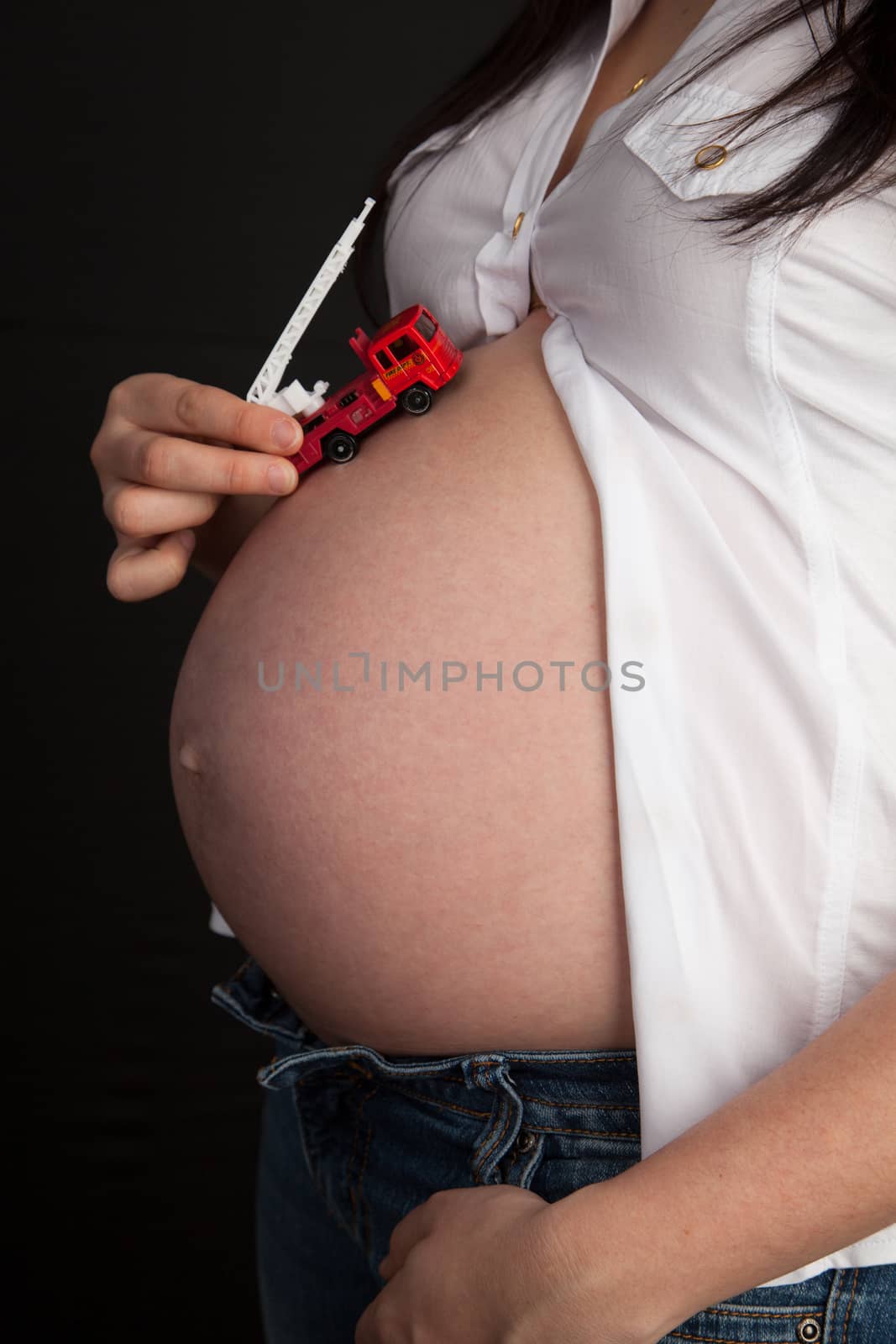 Pregnant woman holding a fire truck on her belly by Izaphoto