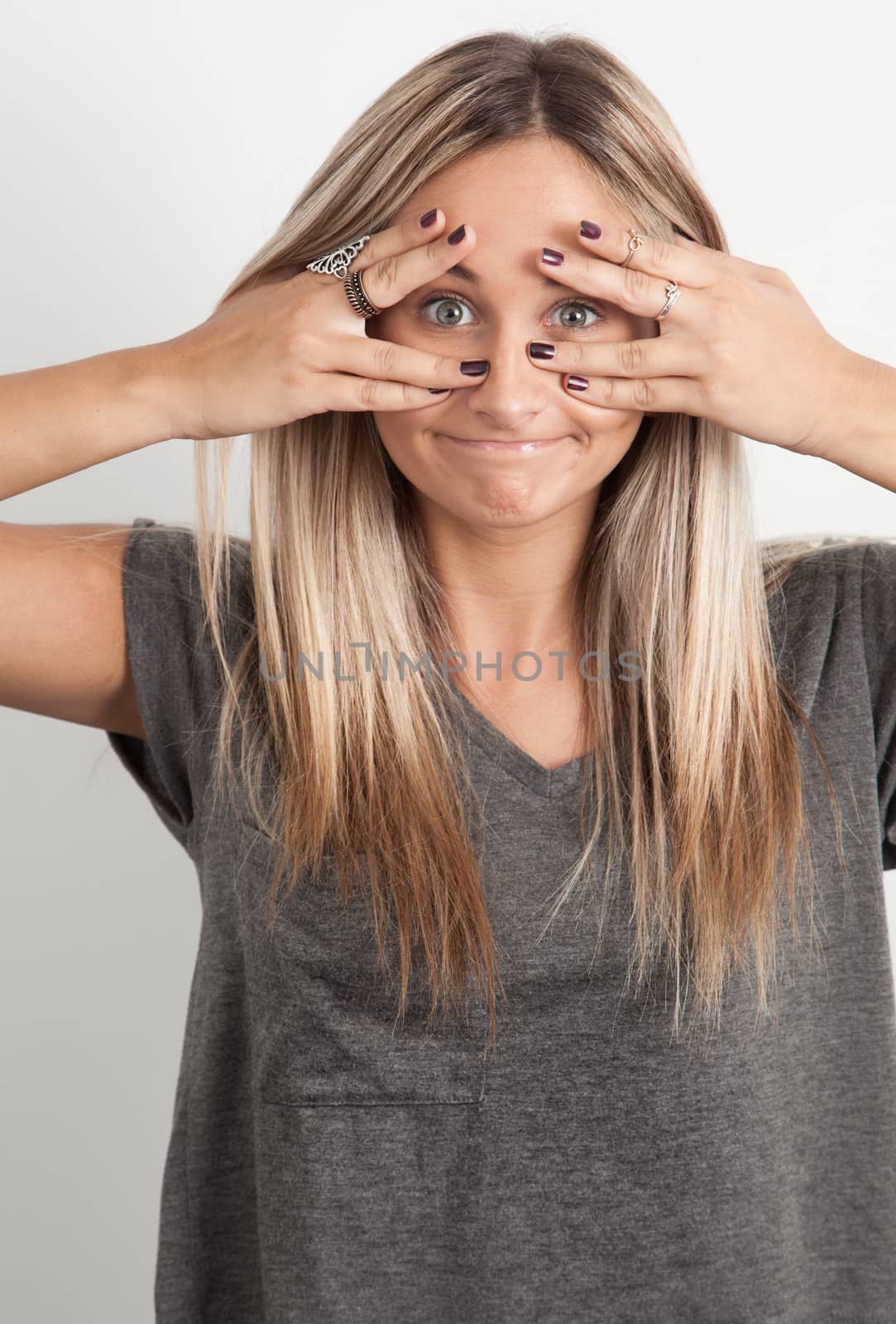 Young caucasian blond Woman Peeking Through Her Hands by Izaphoto