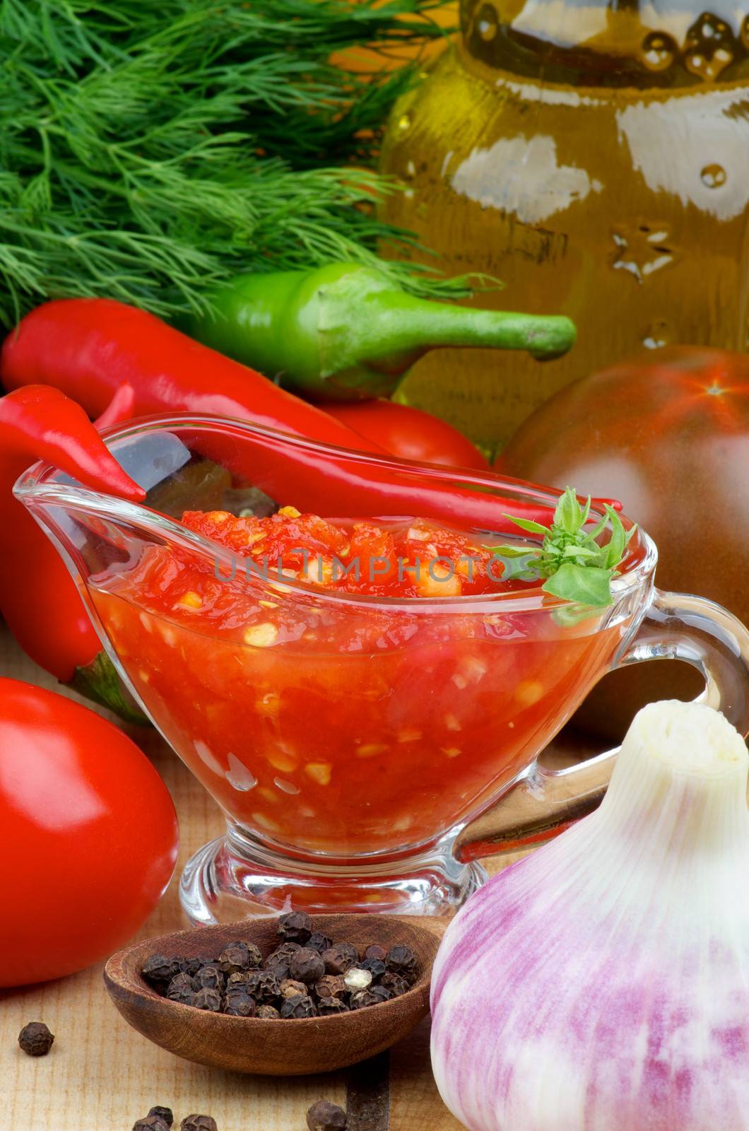 Arrangement of Bruschetta Sauce in Glass Gravy Boat with Black Tomatoes, Garlic, Chili Peppers and Glass Bottle of Olive Oil closeup on Wooden background