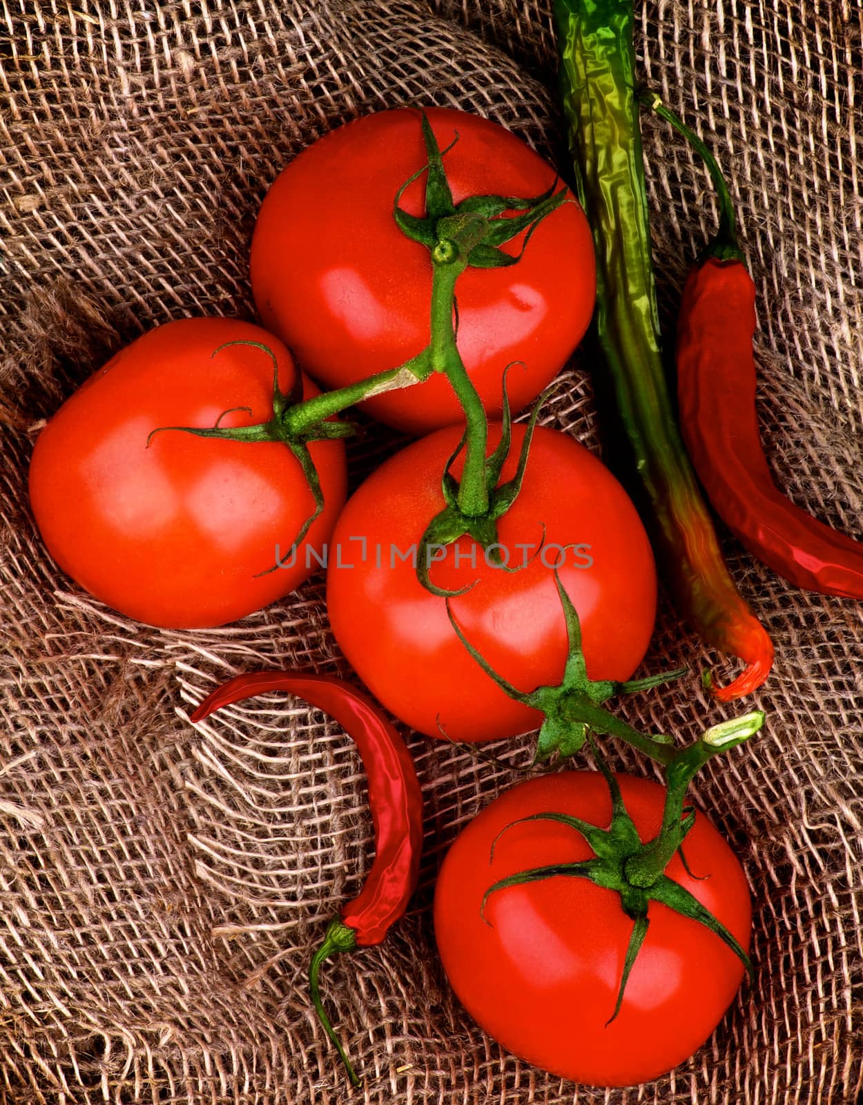 Fresh Ripe Tomatoes with Stems and Chili Peppers closeup on Burlap background. Top View