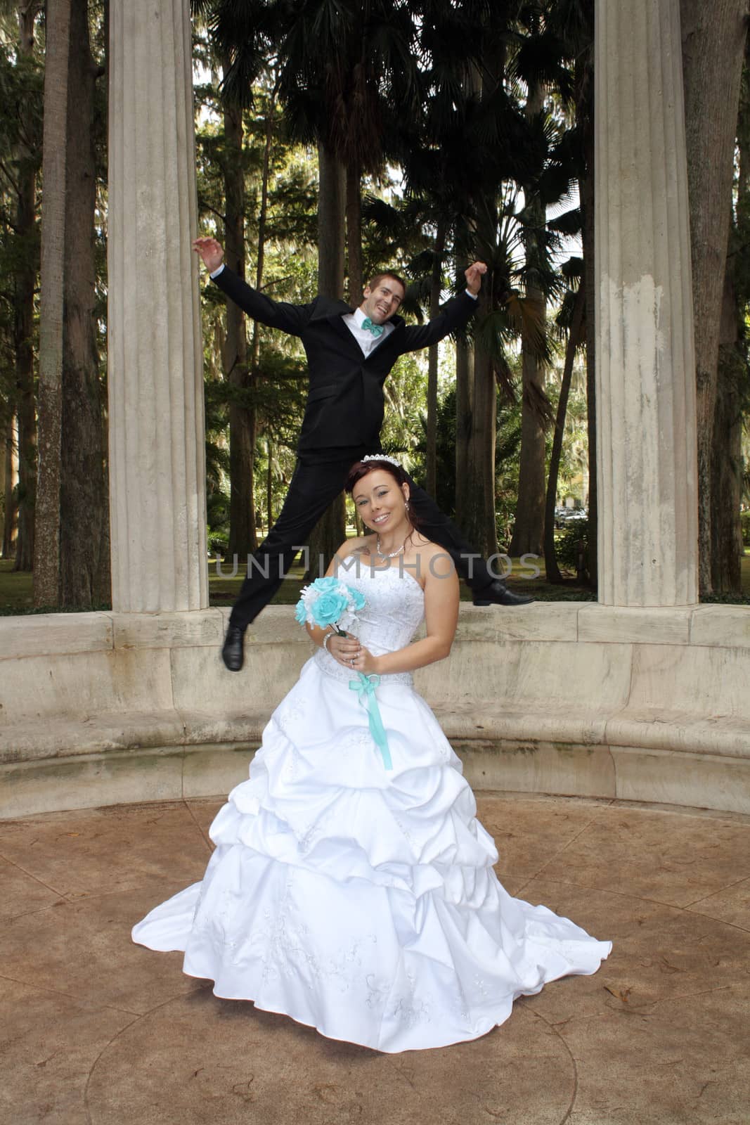 A handsome groom playfully jumps on his bride from behind outdoors.