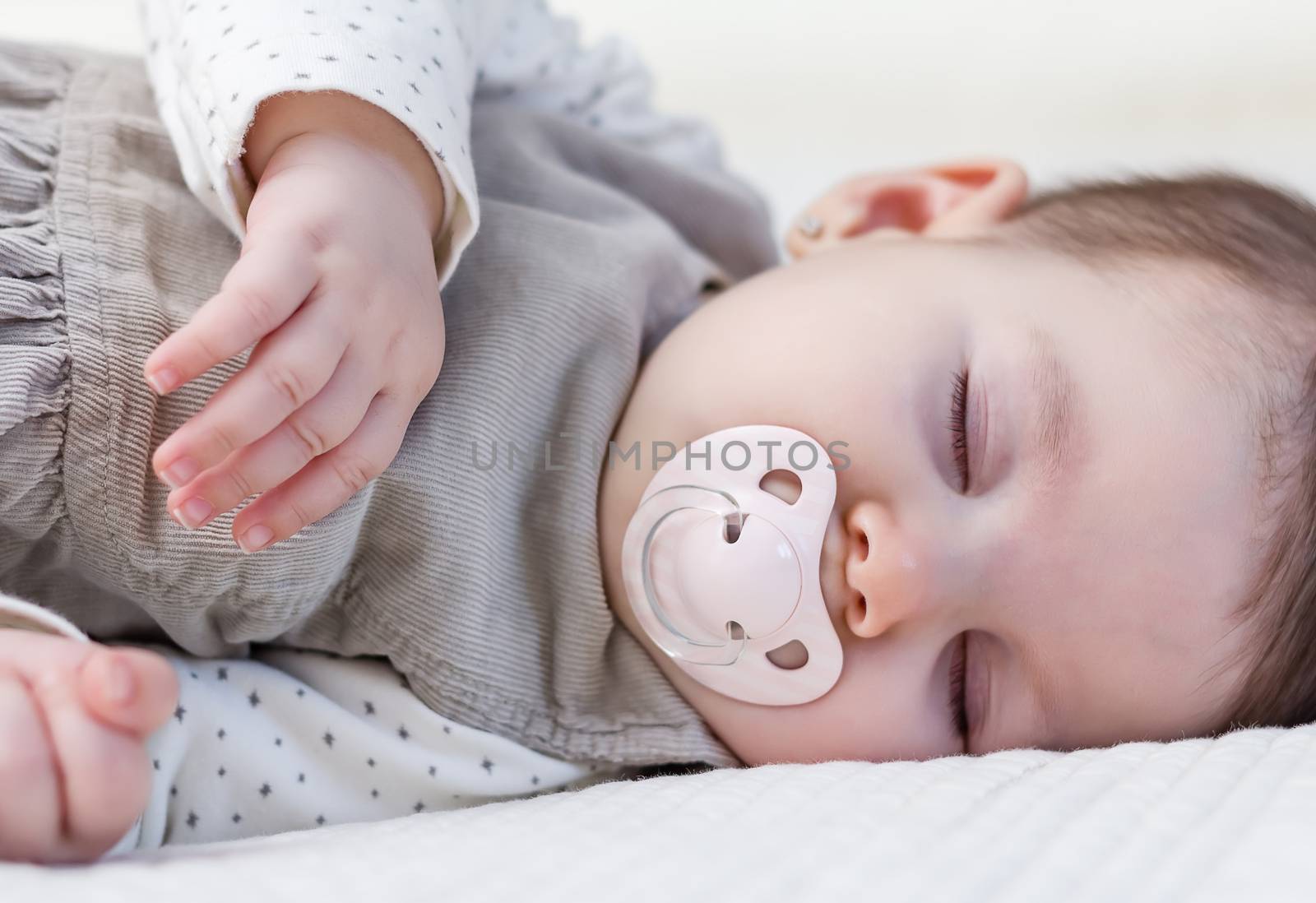 Cute baby girl with pacifier sleeping over white bedcover