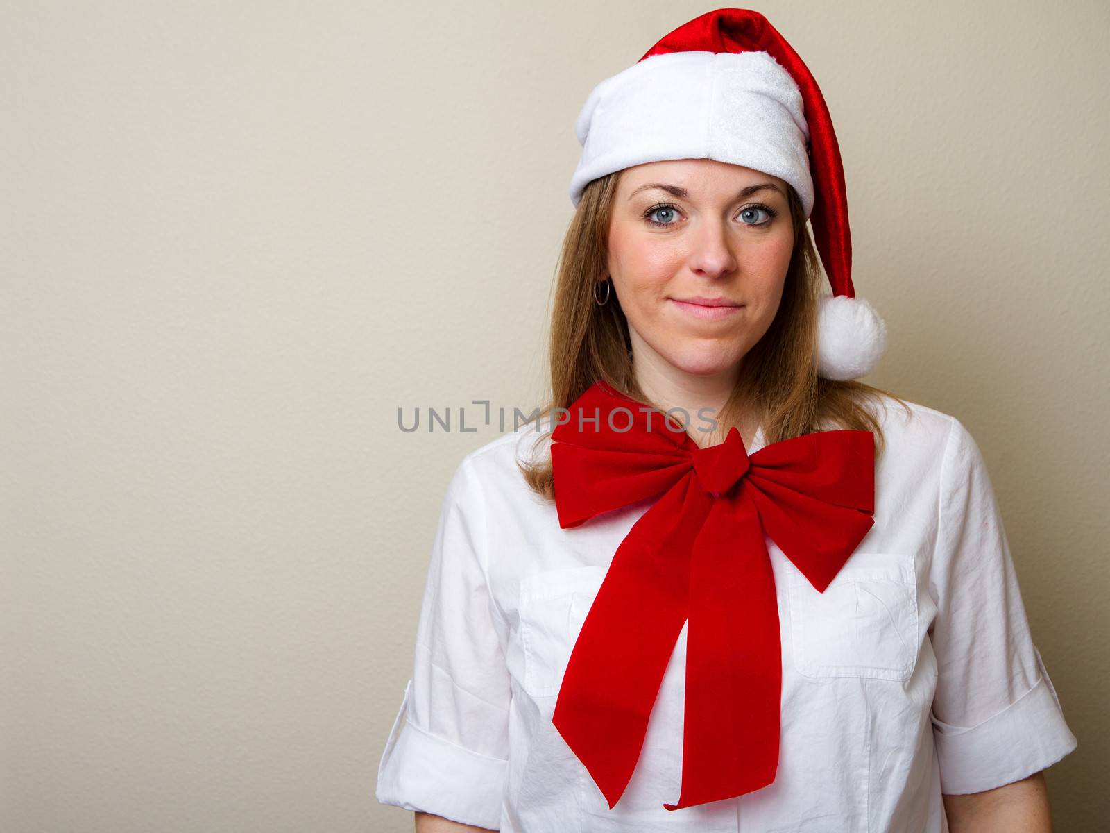Woman with a santa hat smiles at the camera while wearing a bow