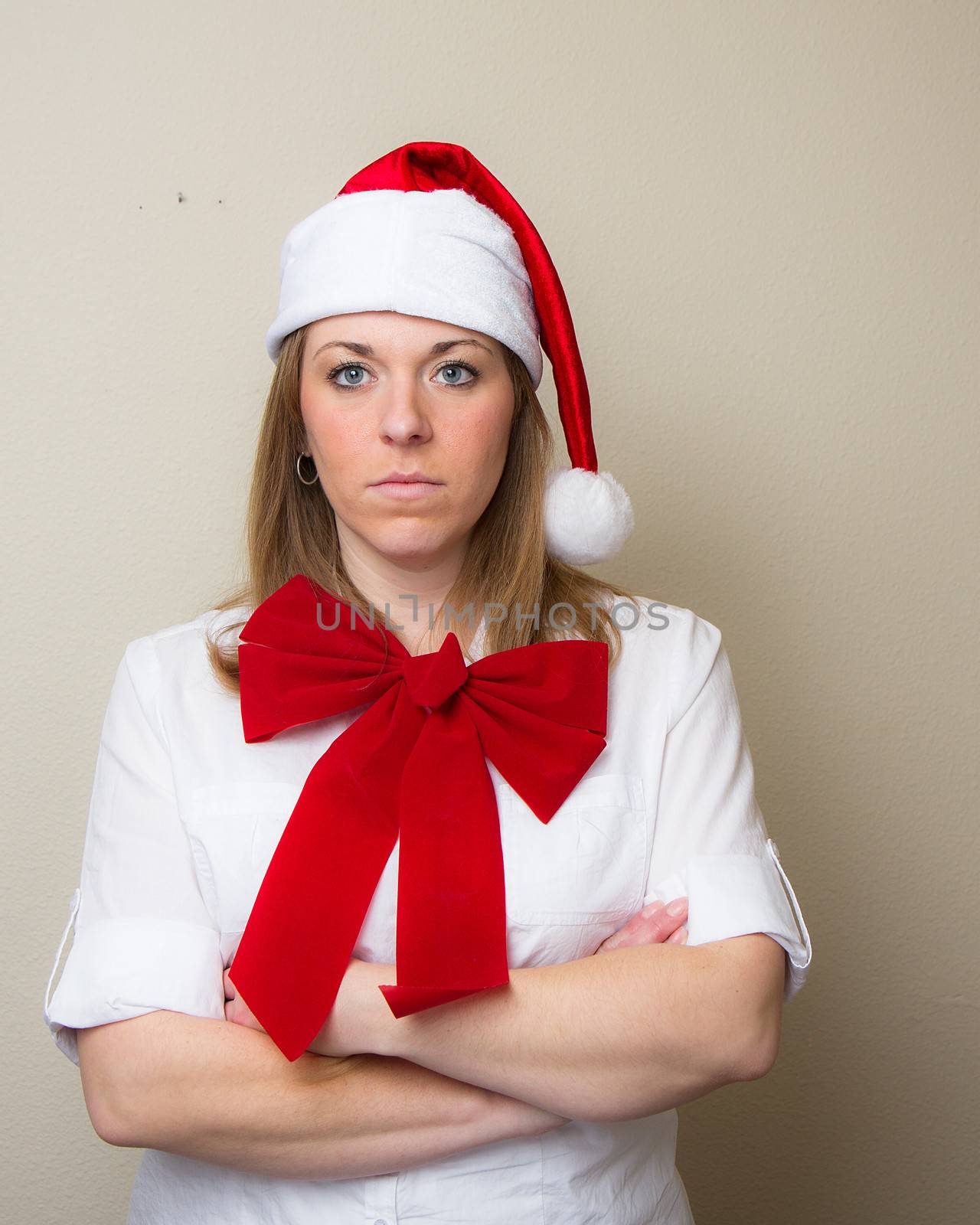 During christmas time a woman in a santa hat and a bow doesn't look happy