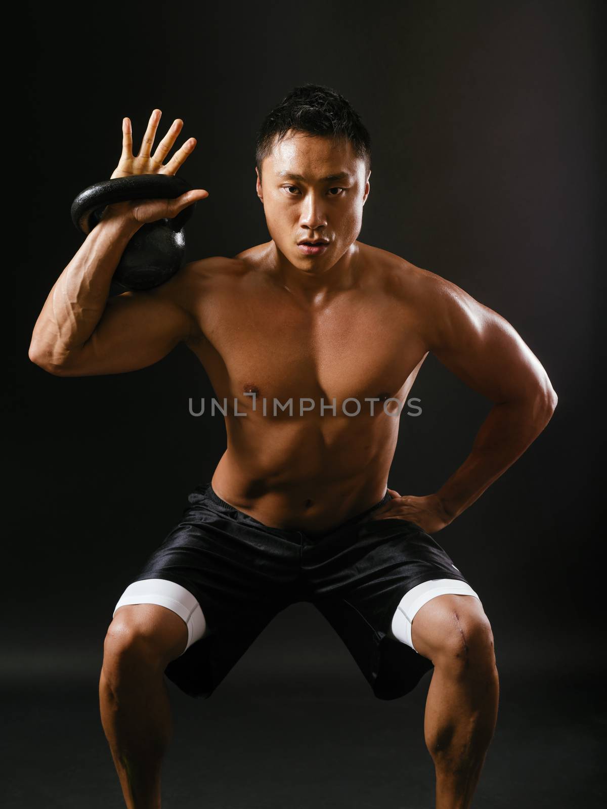 Photo of a muscular Asian man doing squats while holding a kettlebell.
