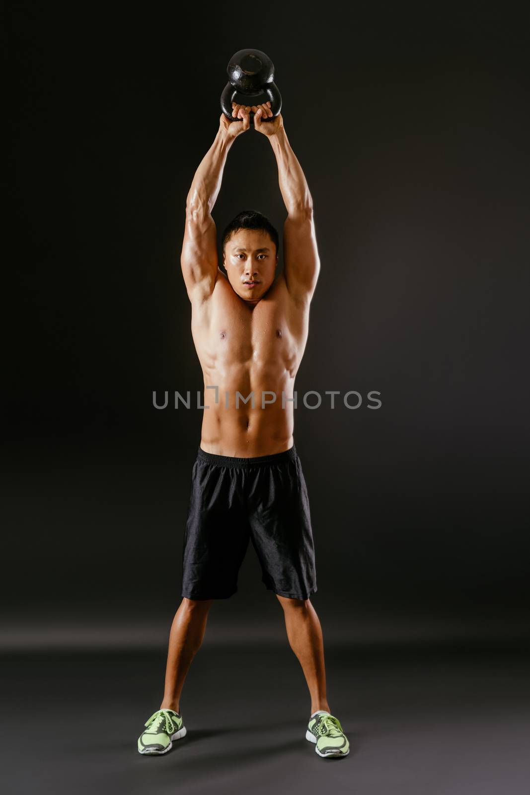 Photo of an Asian male exercising with a kettle bell over dark background. 