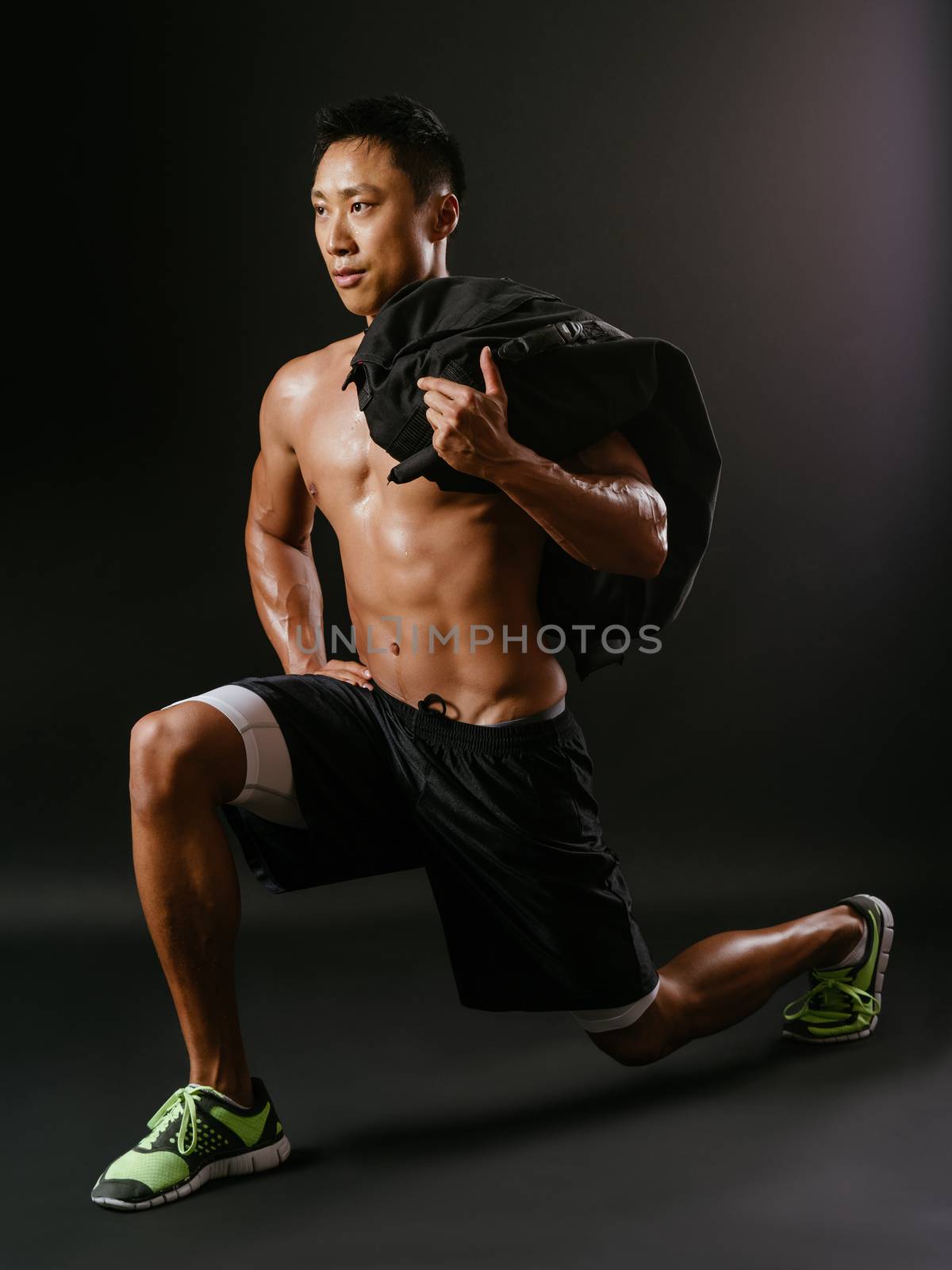 Photo of a muscular man doing lunges with a sand bag.