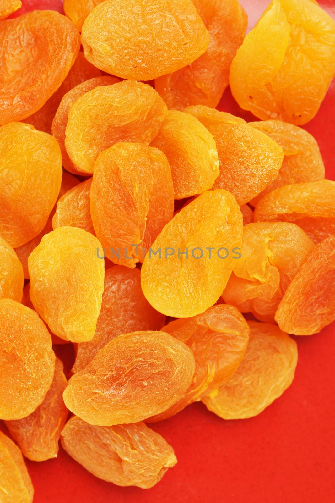 Heap of sweet dried apricot fruits on red plate, colorful food background