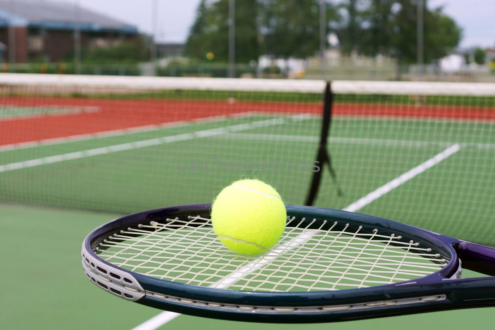 Tennis concept, ball on racket in front of net on hard court
