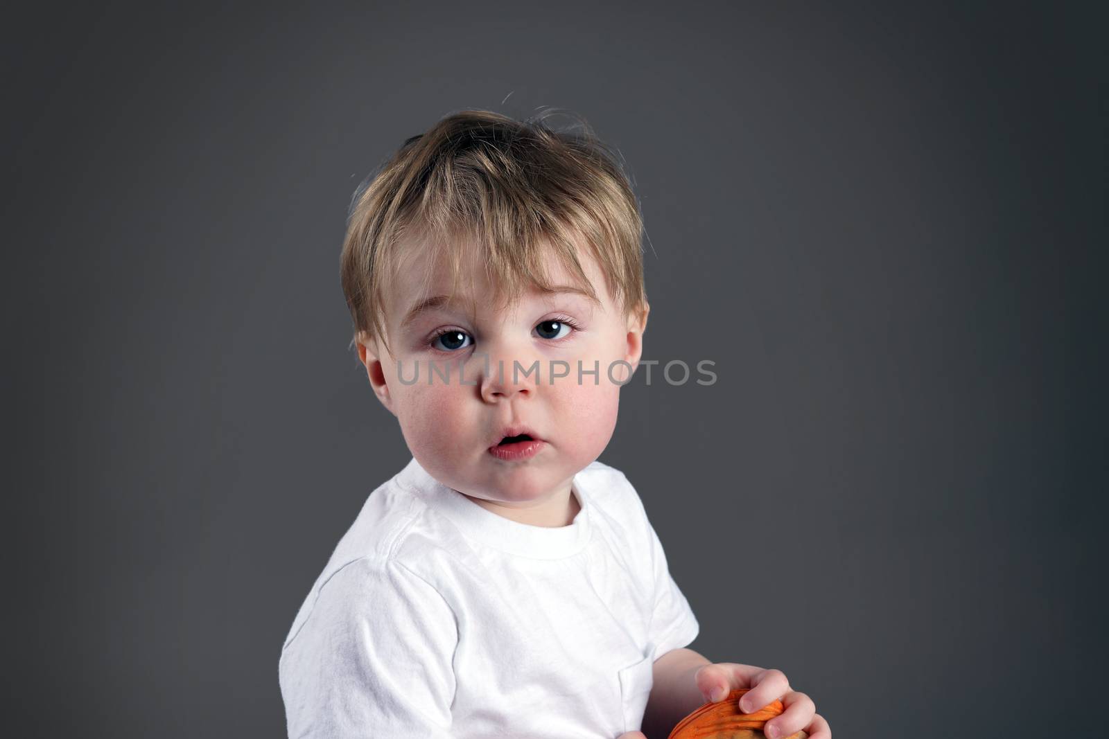 Portrait of little blond boy or toddler looking upset, desaturated on grey background.