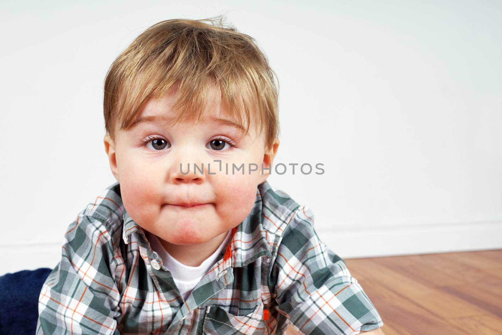 Cute little blond boy or toddler looking at camera while playing on wood floor