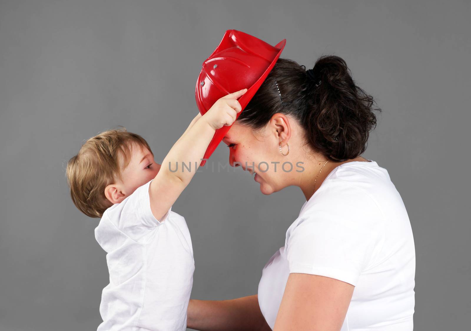 Mother and child playing, little blond boy or toddler putting a red plastic fireman's hat on mom