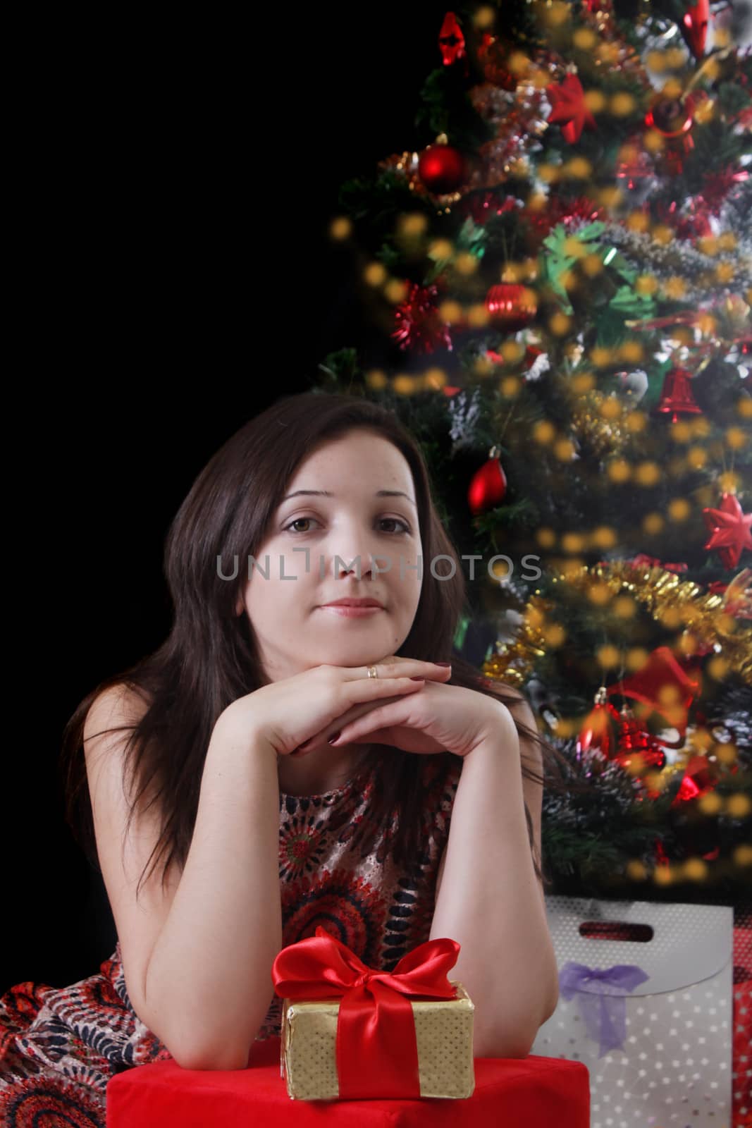 Pretty woman with gifts under Christmas tree on balck