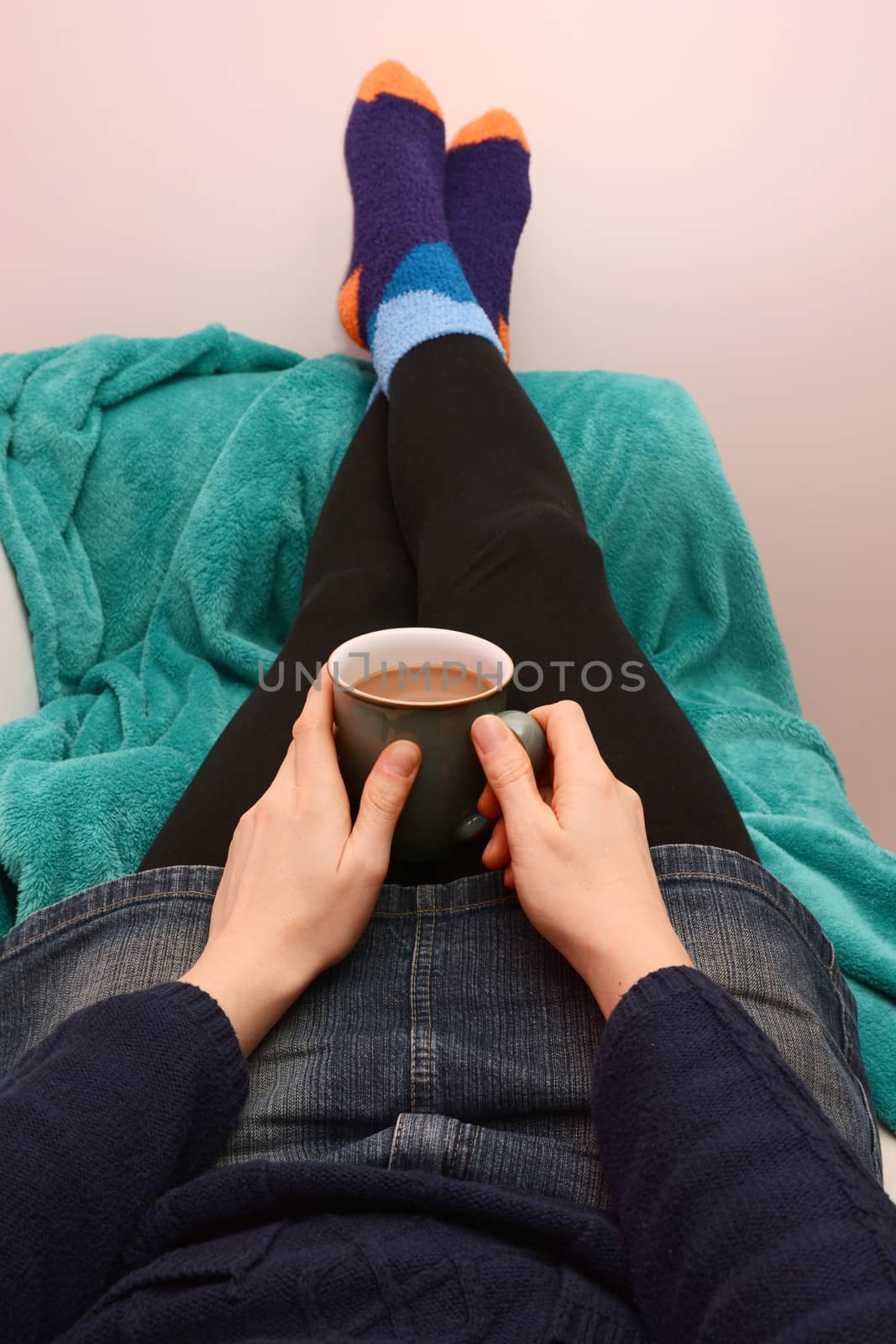 Woman holding a cup of coffee or tea, relaxing on the couch with her feet up