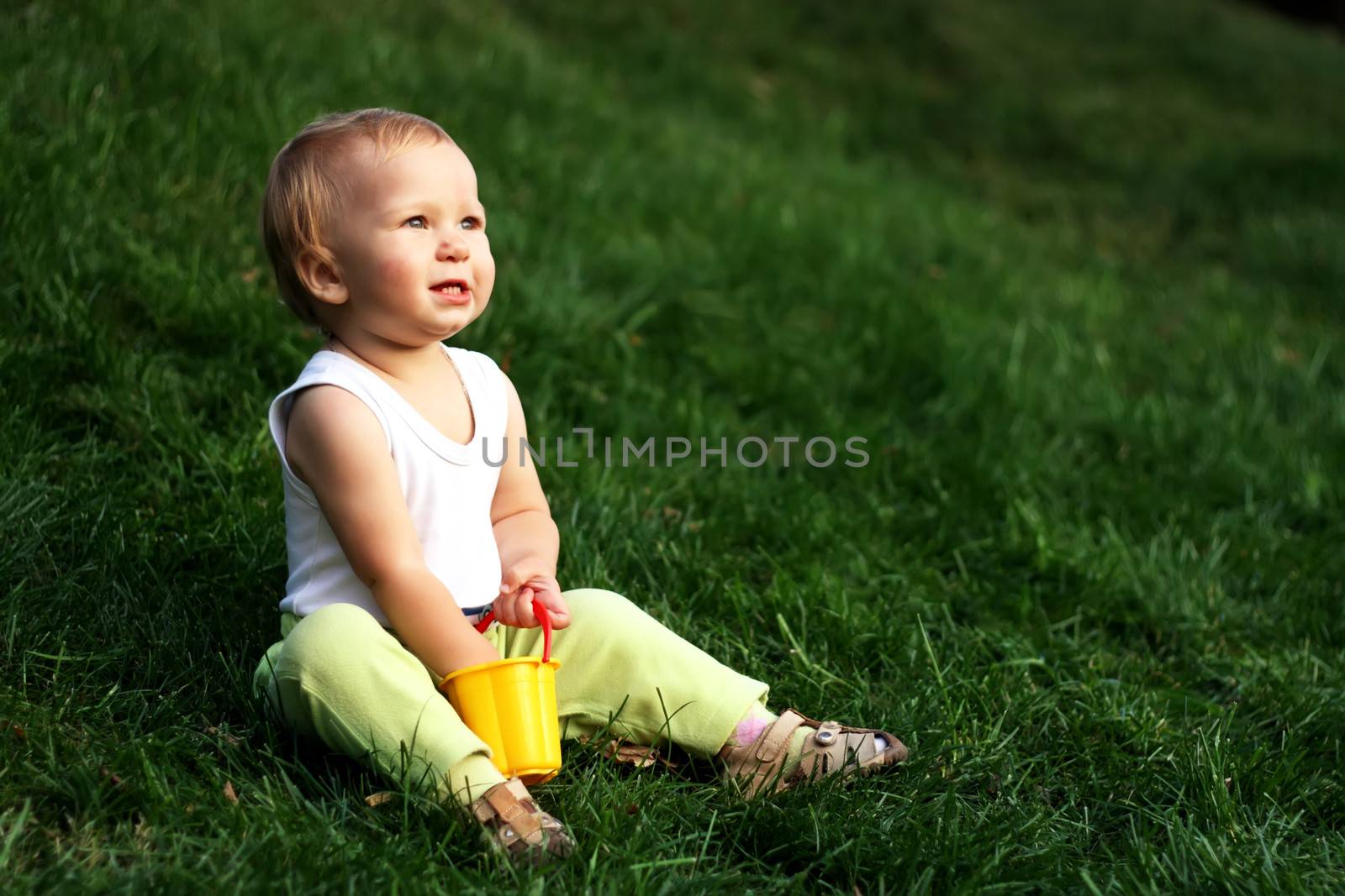 Little boy with pail sits on a green grass 