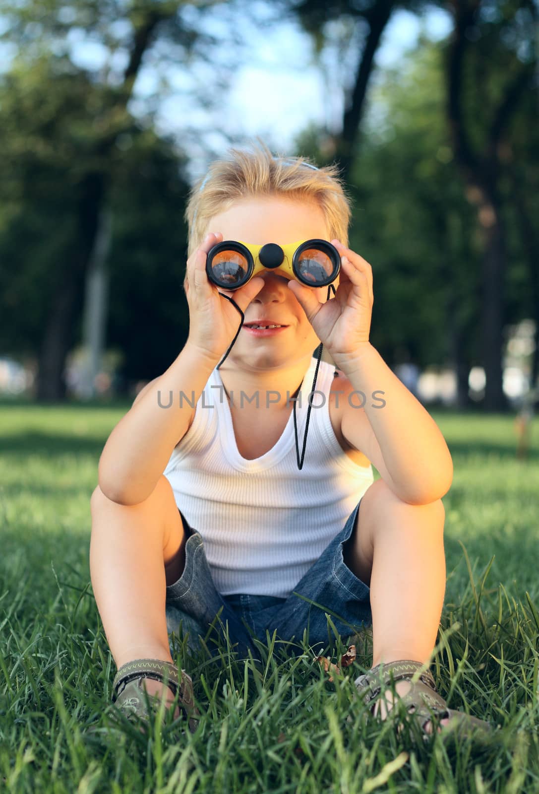 Little boy sitting in the park with a binoculars by dedmorozz