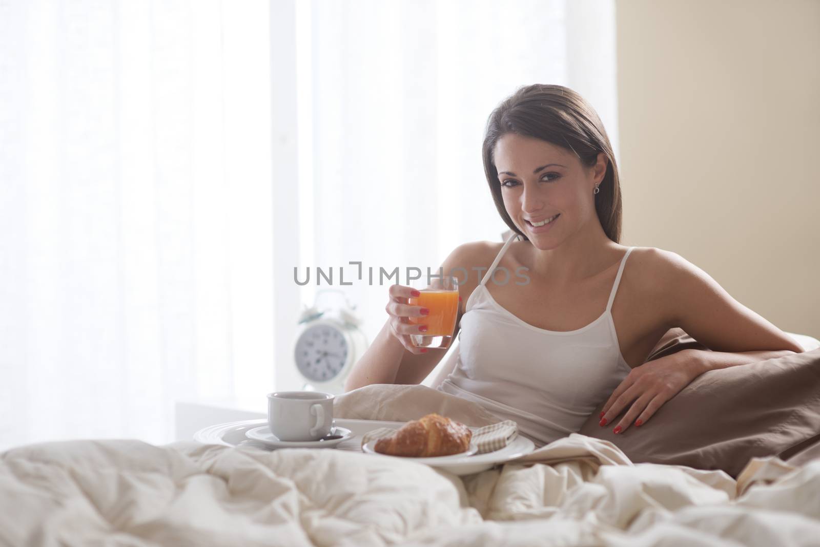 Lovely young woman lying with a glass of orange juice and a tray of breakfast 