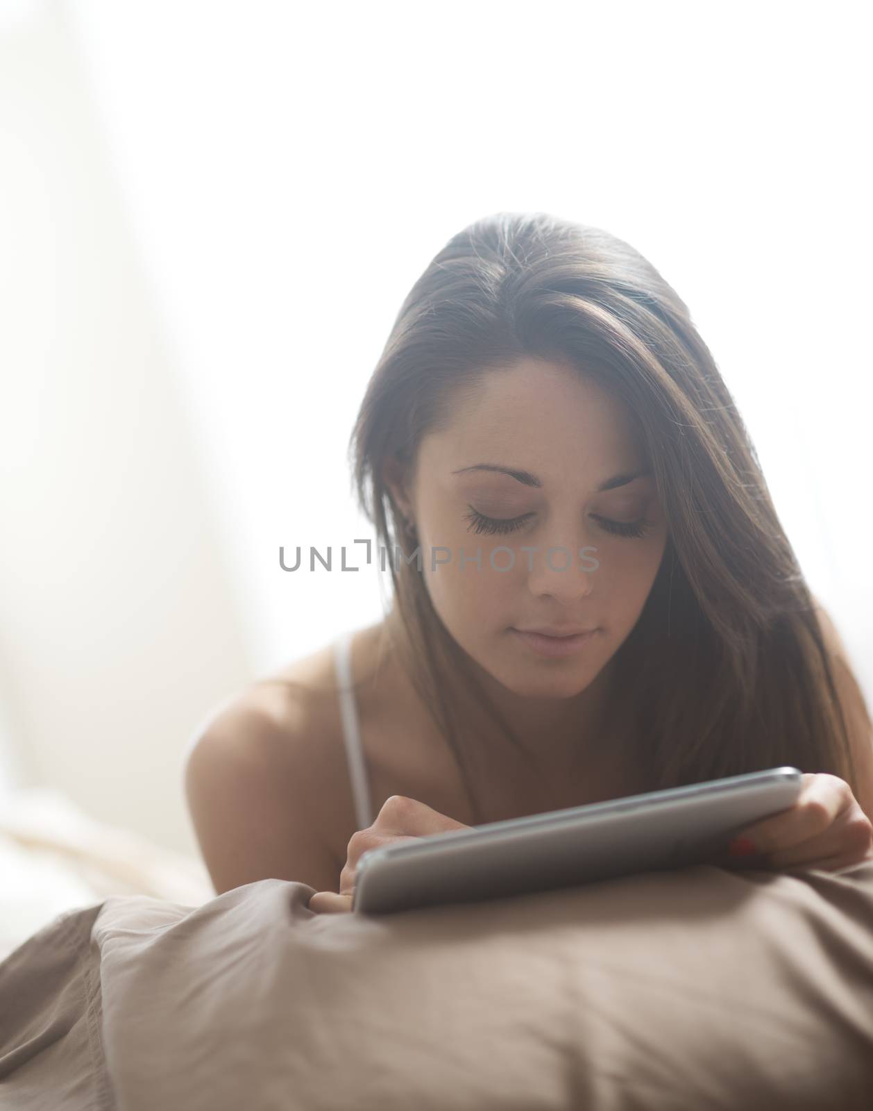 An attractive young female lying on her bed using a tablet 