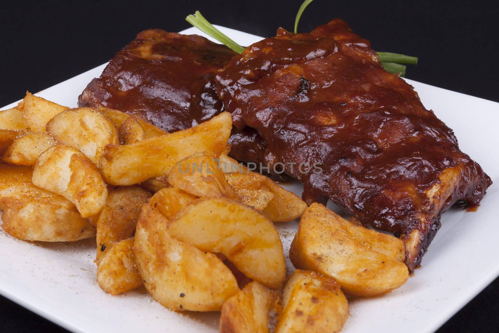 Close up BBQ ribs with potato wedges on a white plate.