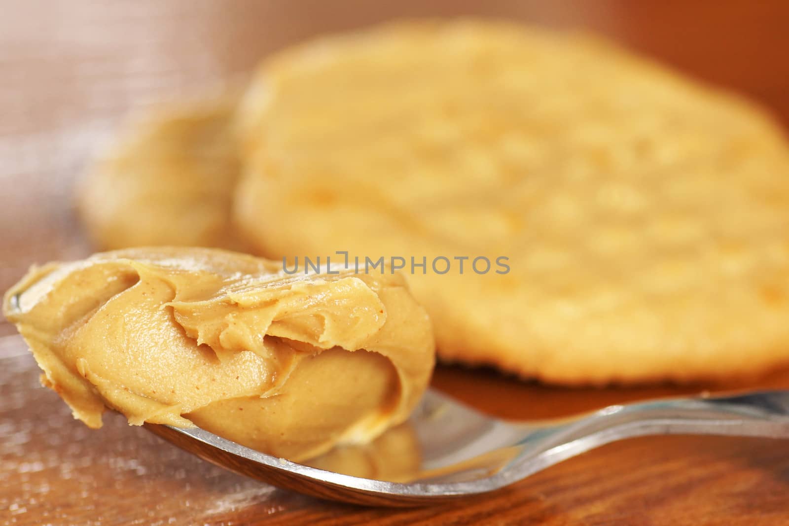 Spoon full with smooth peanut butter, cookies in the background on wooden table.