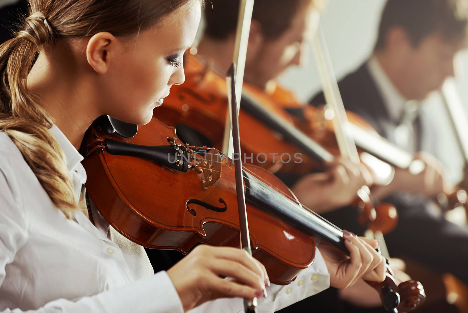 Violinists playing at the concert, young beautiful woman on foreground