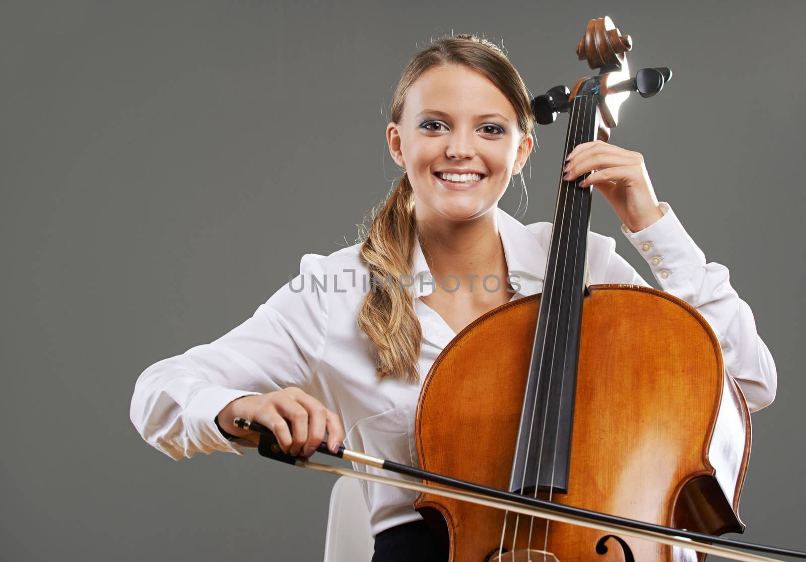 Smiling young woman cellist on grey background