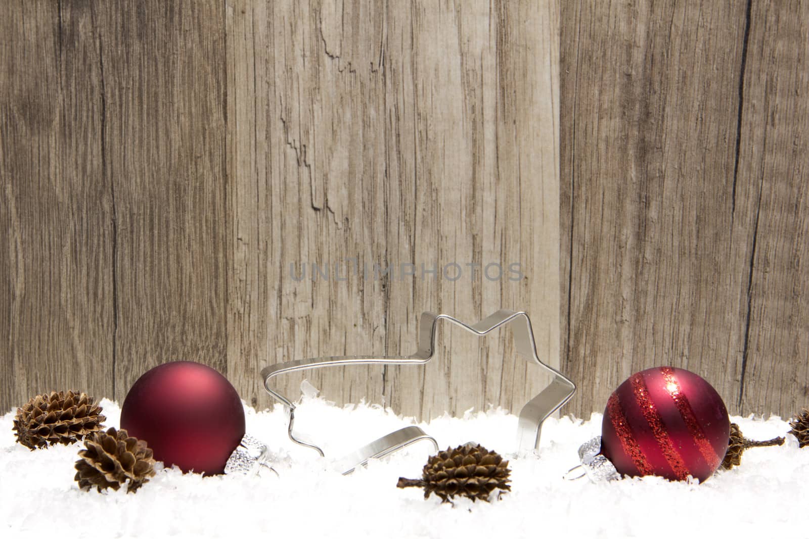 christmas decoration with wooden background, snow, christmas baubles red, shooting star, and pine cones 