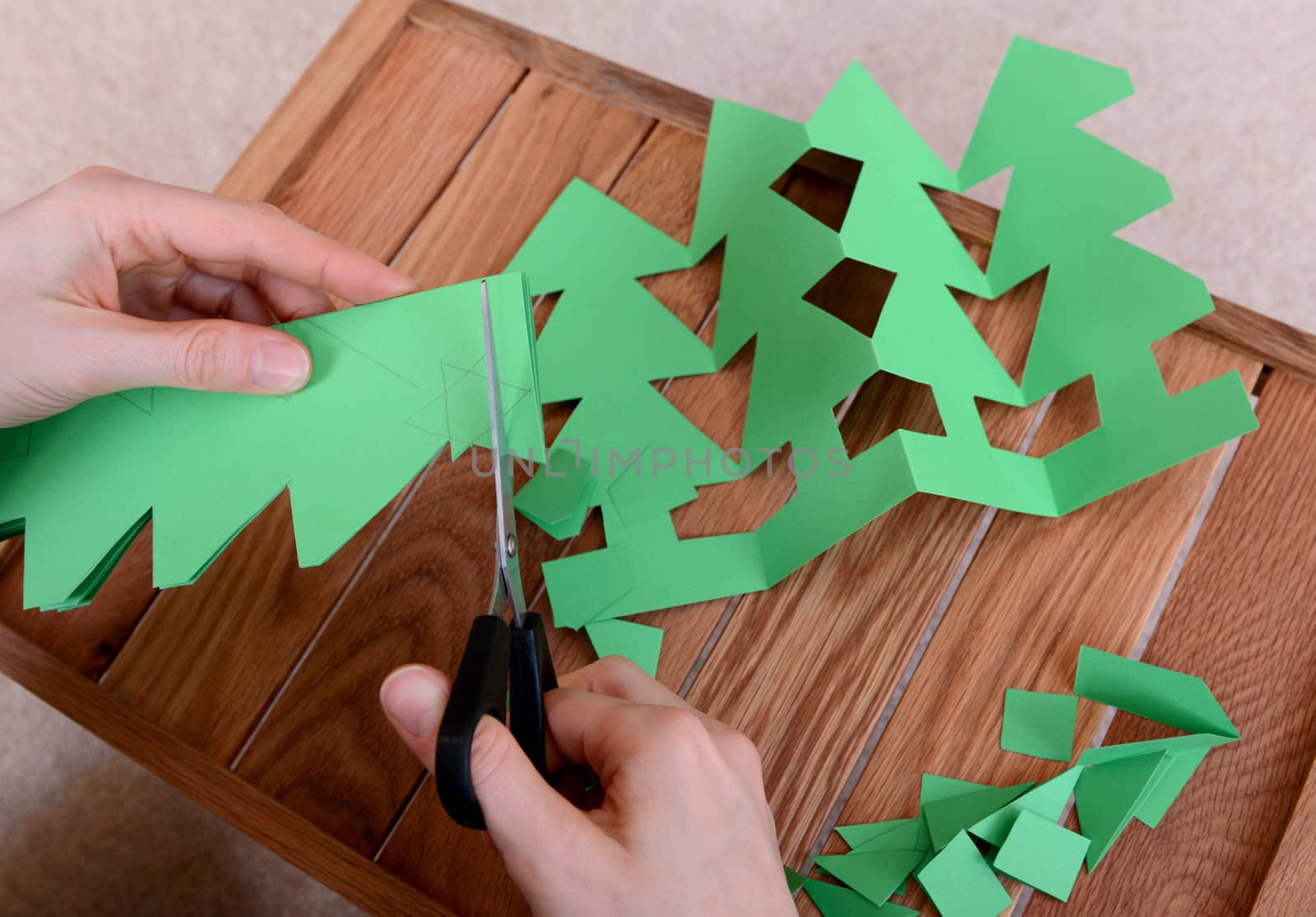 Cutting green card with scissors to make a chain of Christmas trees