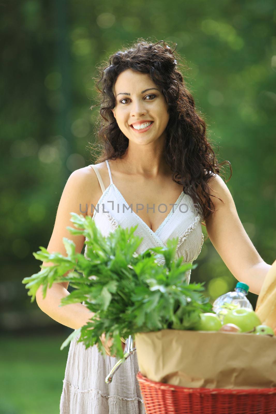 Portrait of pretty young woman with bicycle and groceries in a park 