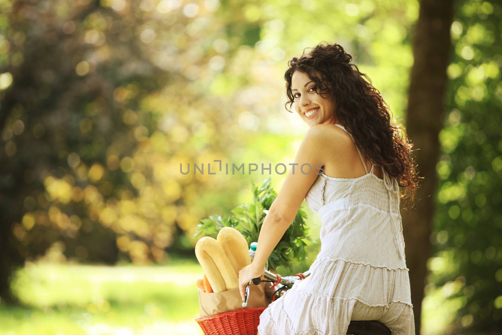 Portrait of a smiling young woman riding bicycle with groceries in basket
