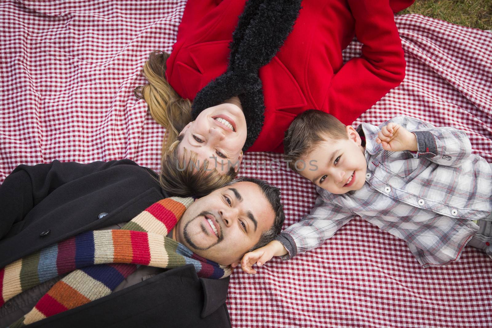 Young Mixed Race Family in Winter Clothing Laying on Their Backs on Picnic Blanket in the Park Together.