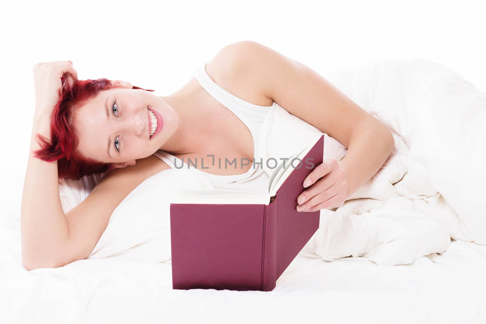 happy redhead woman in bed reading a book on white background
