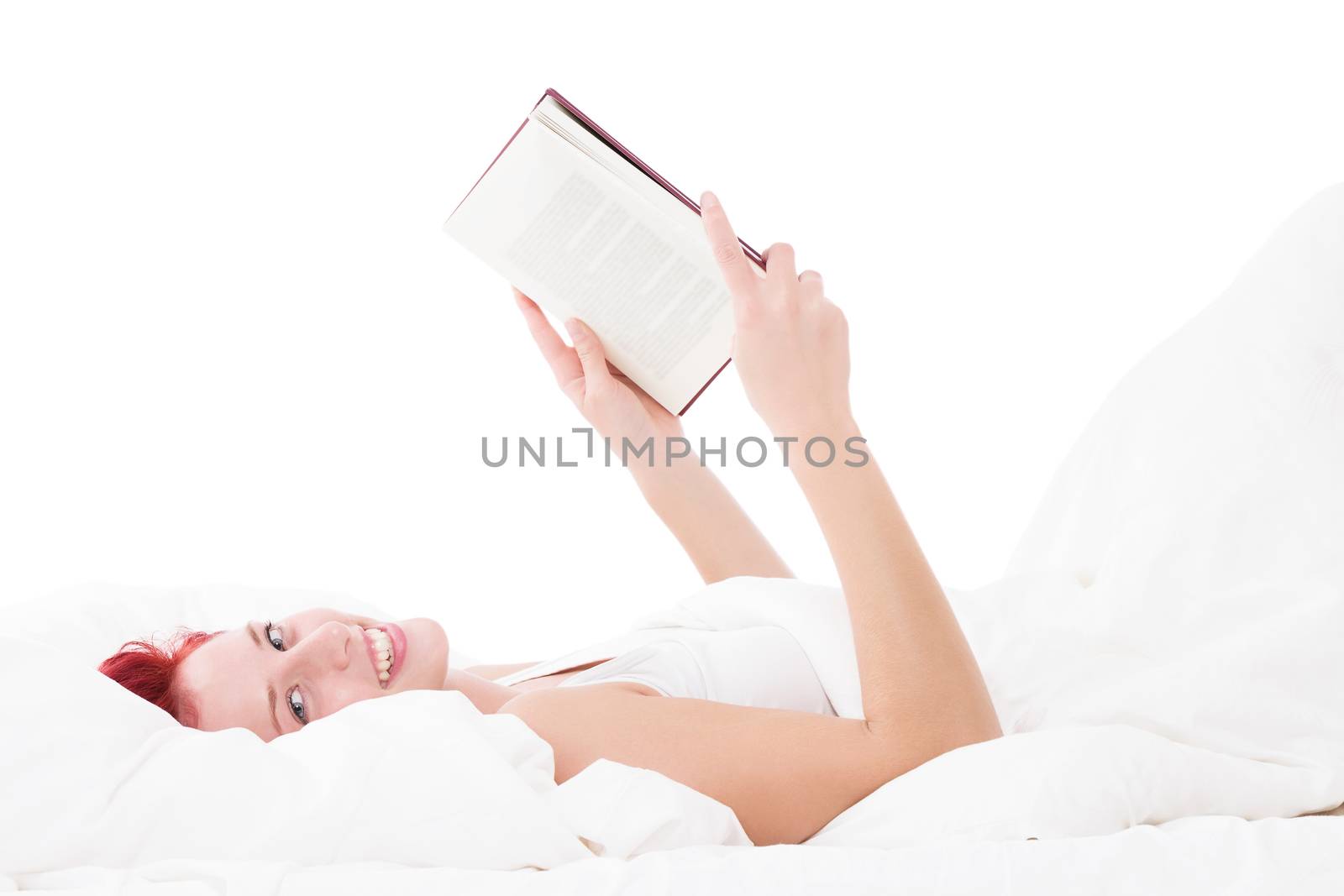 happy redhead woman in bed reading a book on white background