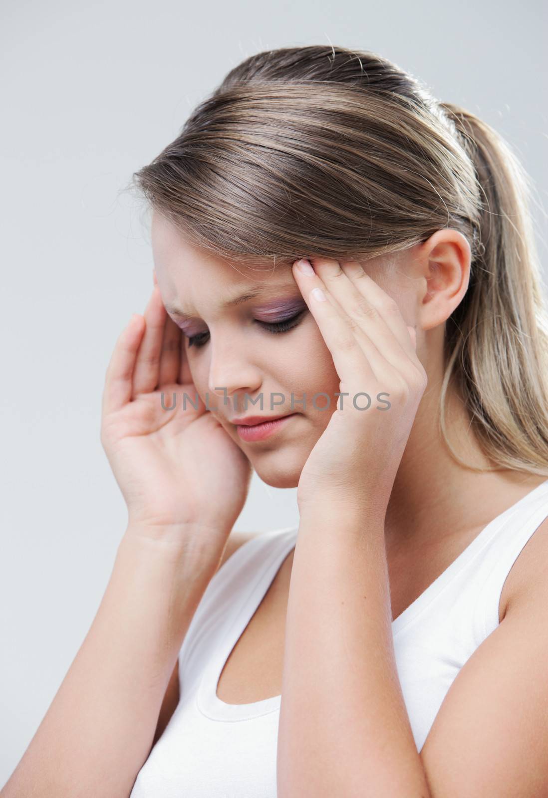 An attractive young woman with her eyes closed is rubbing at her temples to relieve a headache