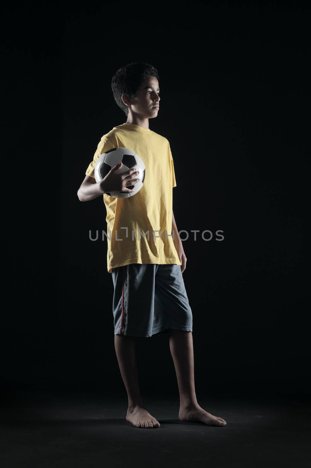 Portrait of young boy with a soccer ball on black background