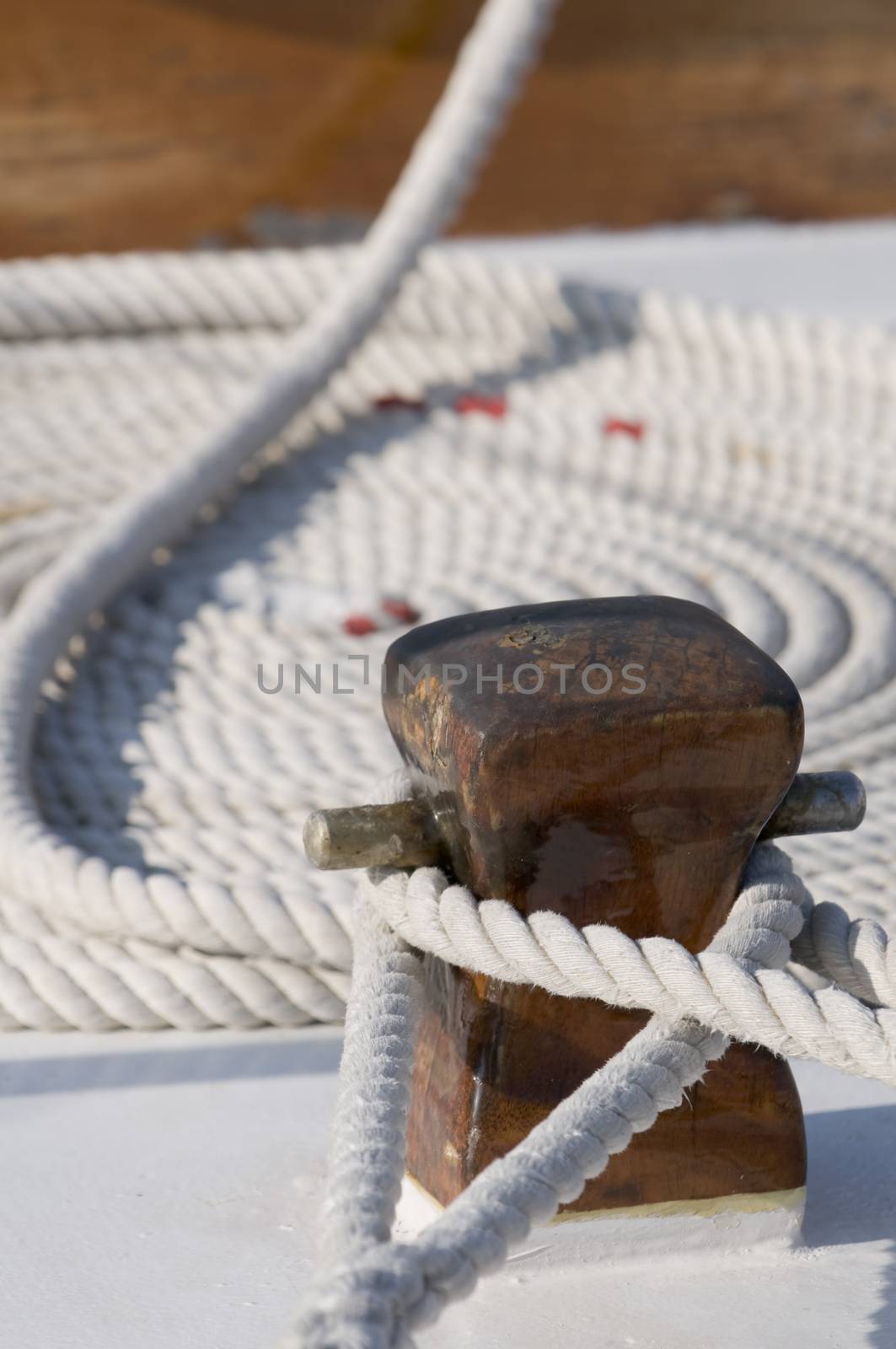 Detail of a sailboat deck with two ropes tied up on a bitt and one rolled rope in background