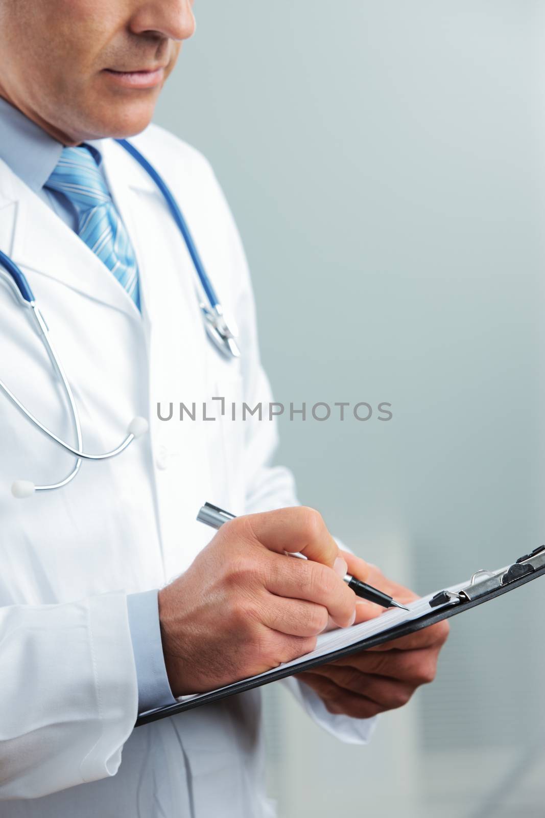 Close up shot of a male doctor writing on clipboard 