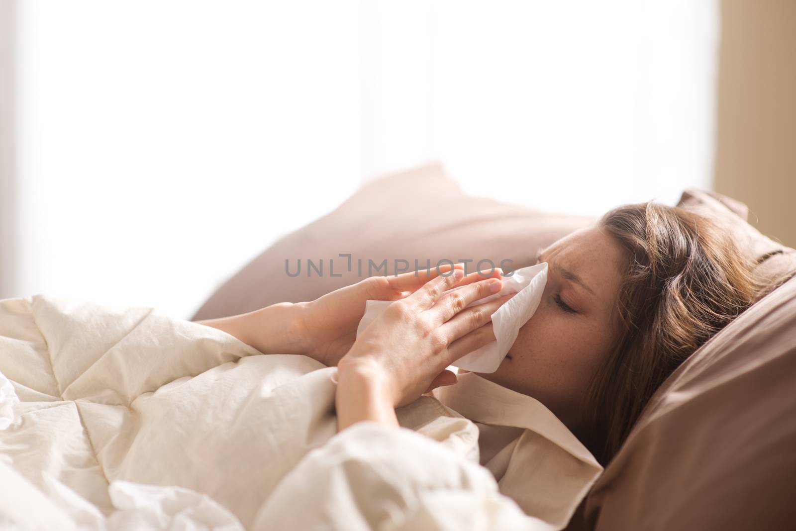 Young sick woman blowing her nose while in bed