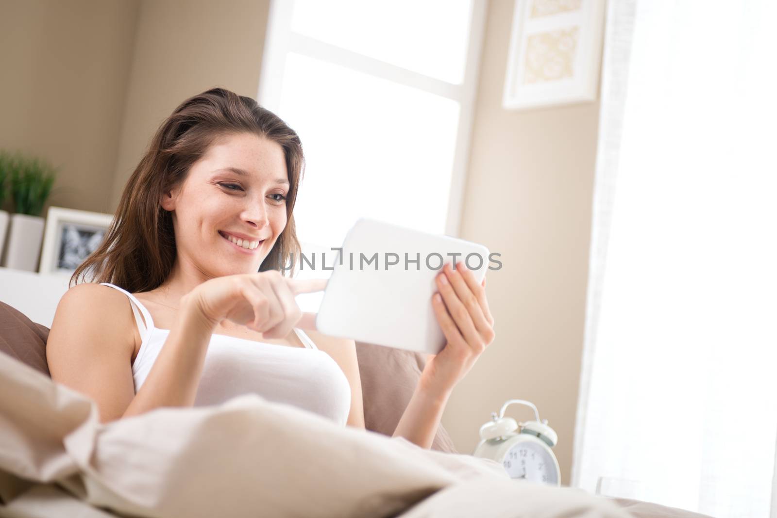 An attractive young female lying on her bed using a tablet 