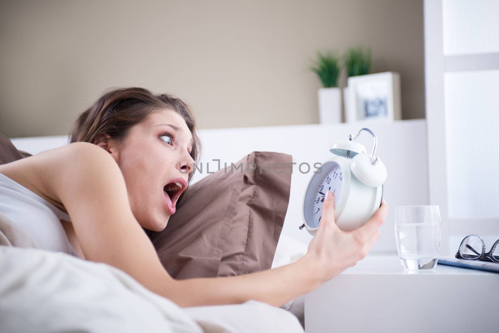 Upset woman holding her alarm clock with an expression of fright