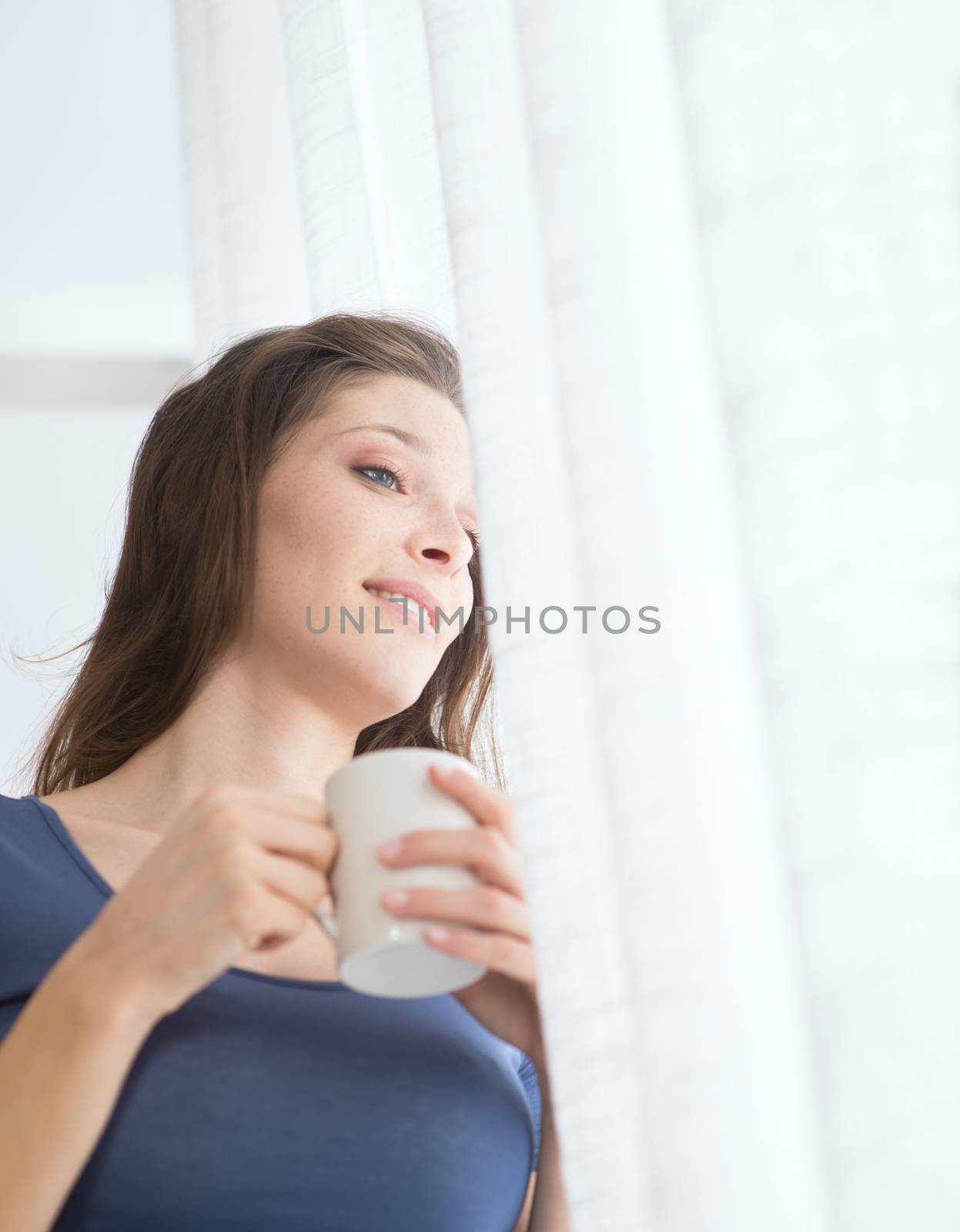 Beautiful woman with cup of coffee looking out of window. 