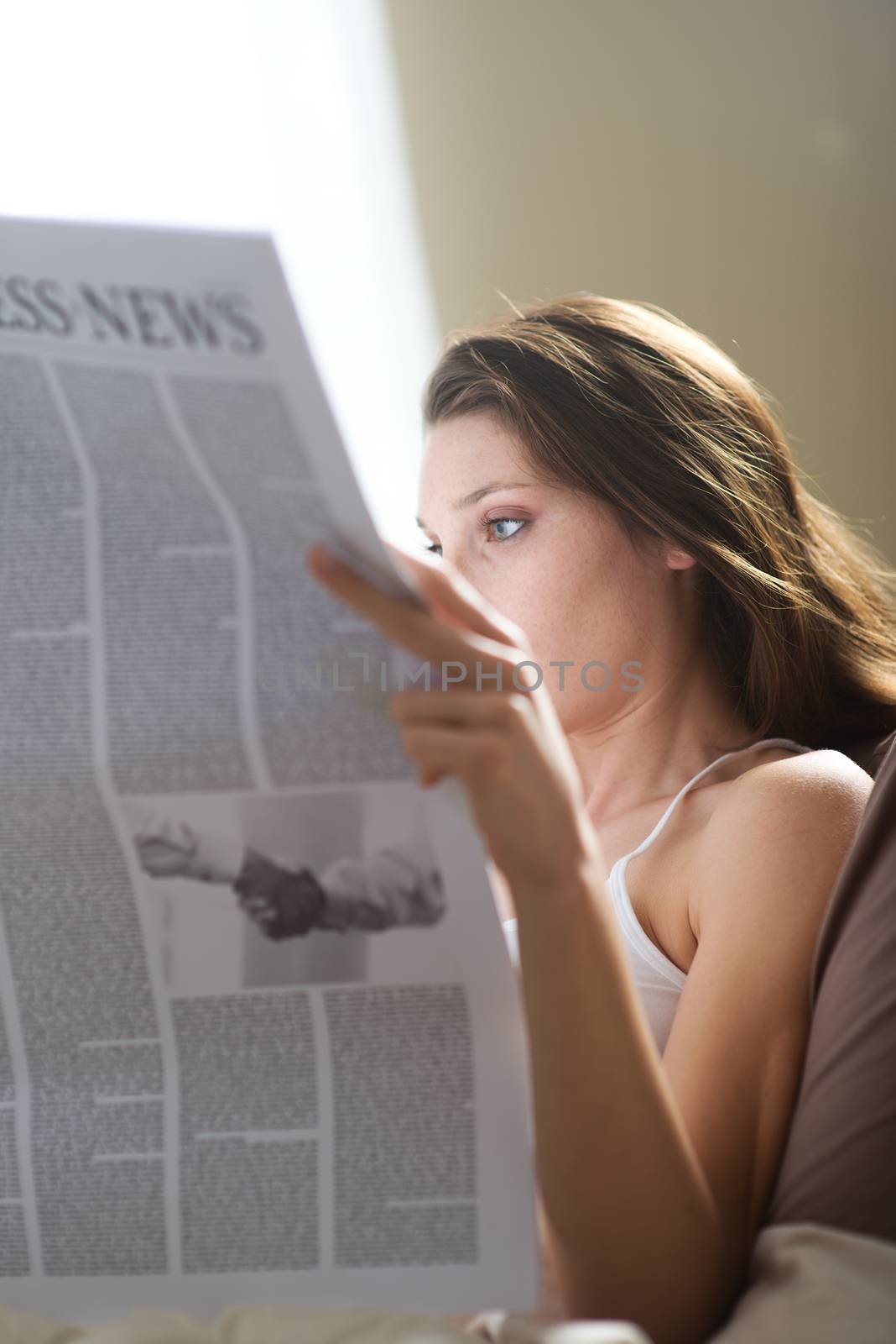Young woman lying on the bed at home and reading the newspaper 