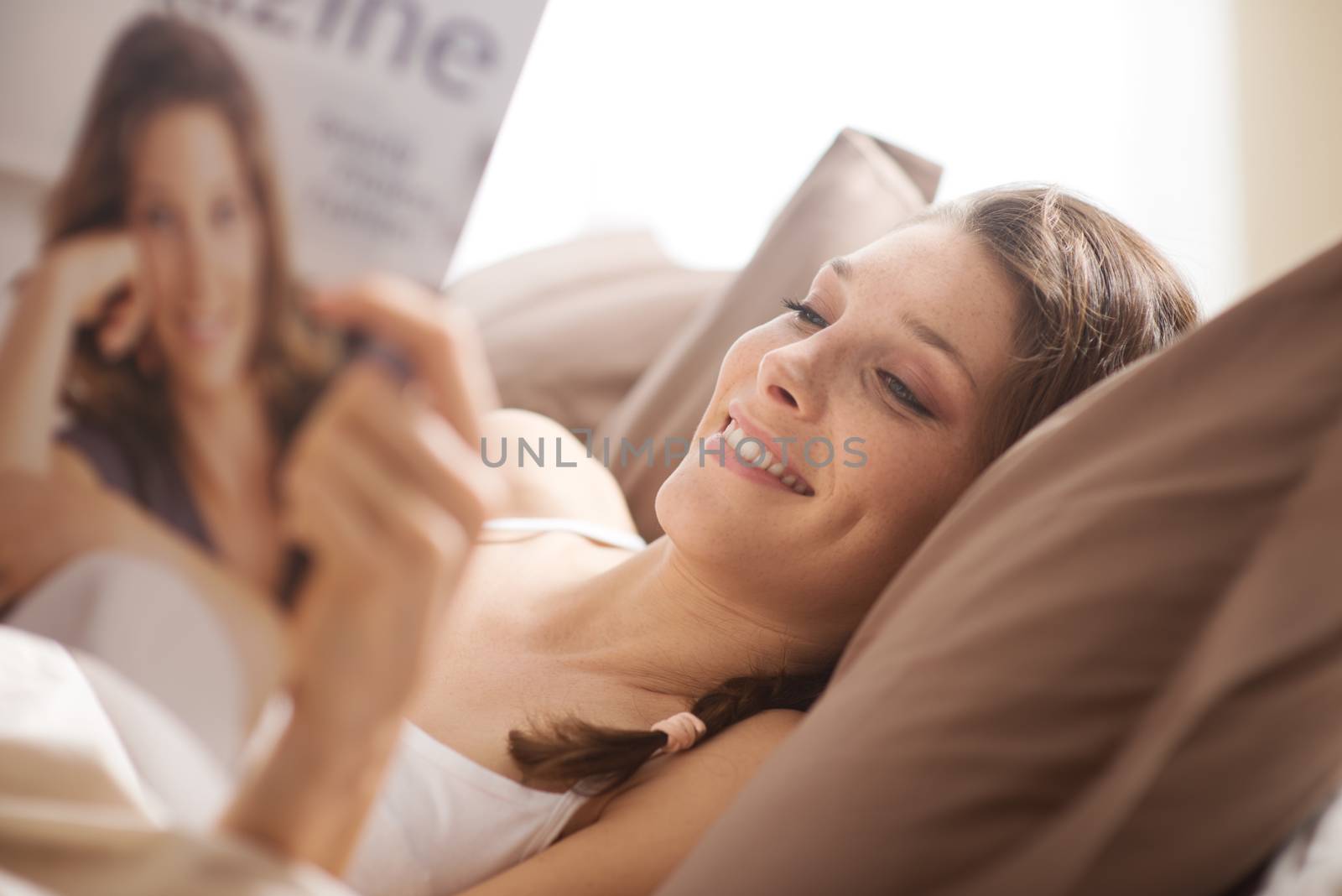 Woman relaxing in bed with magazine by stokkete