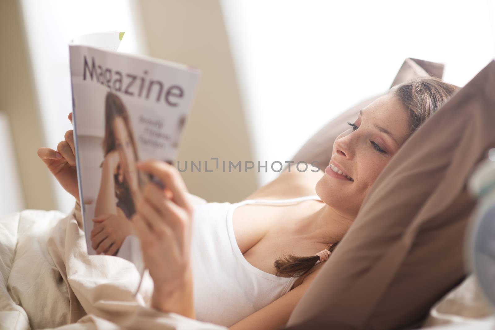 Woman relaxing in bed with magazine by stokkete