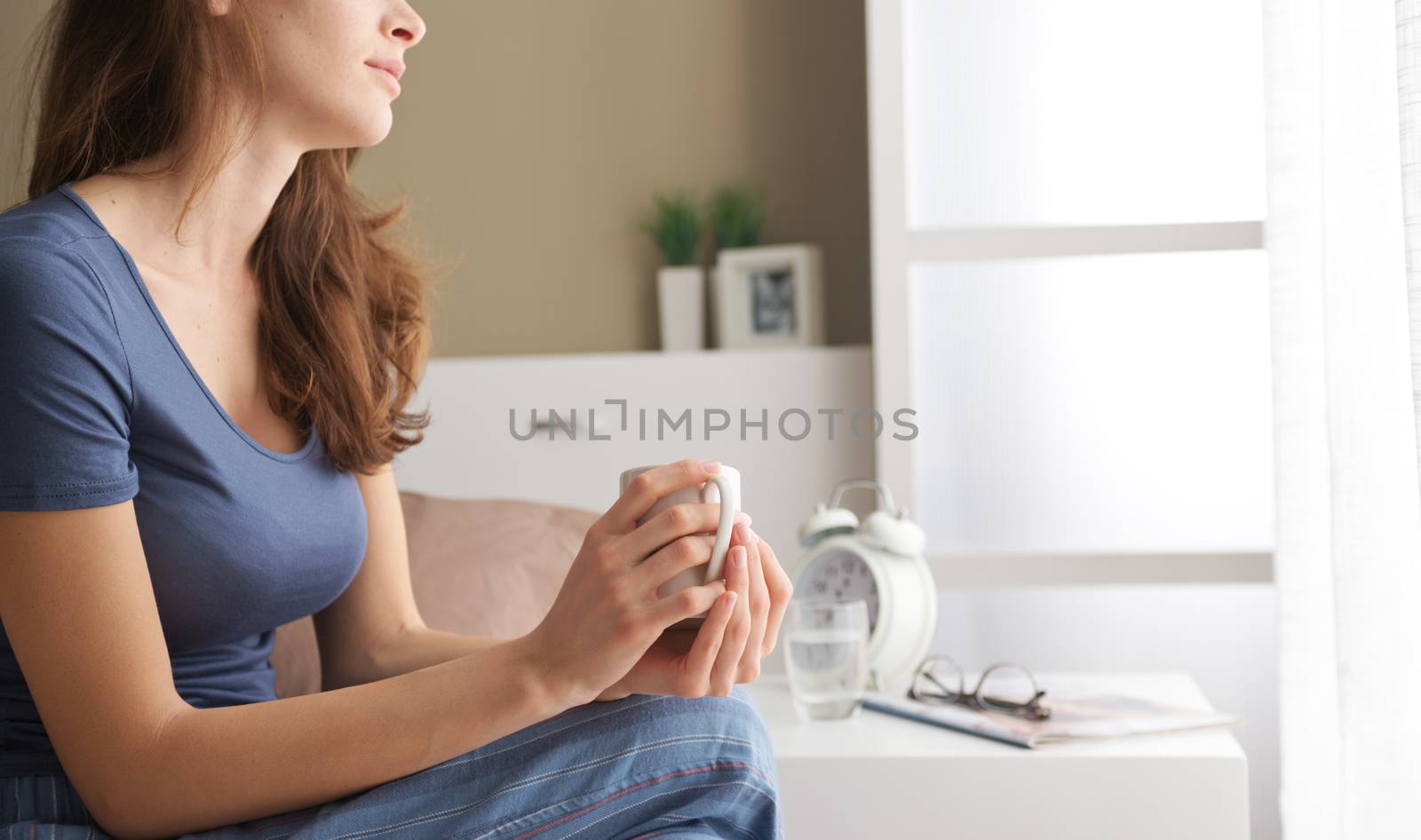 Portrait of a pretty young woman holding a cup of coffee in bed