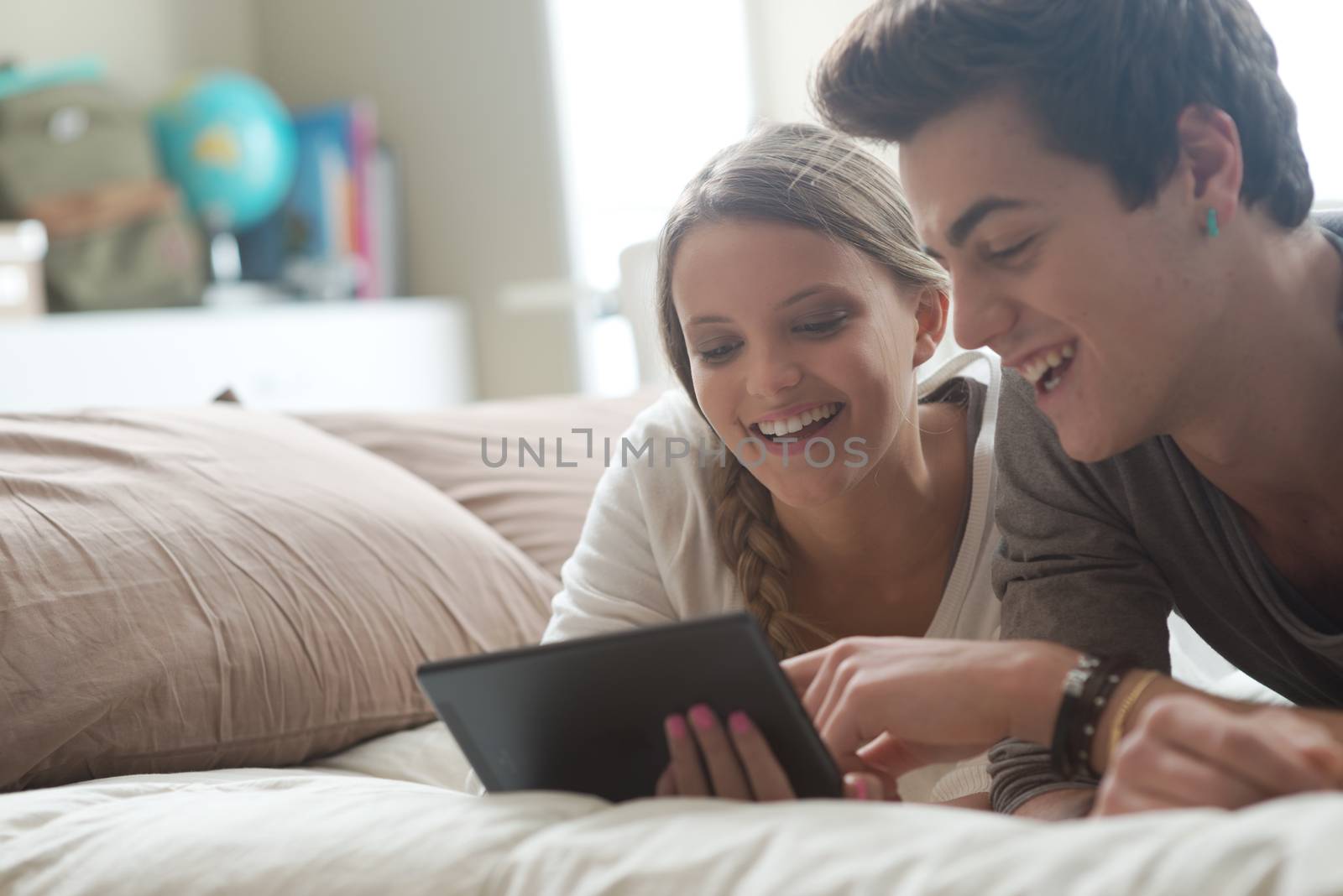 Happy young couple lying on the bed in a bedroom and using digital tablet.