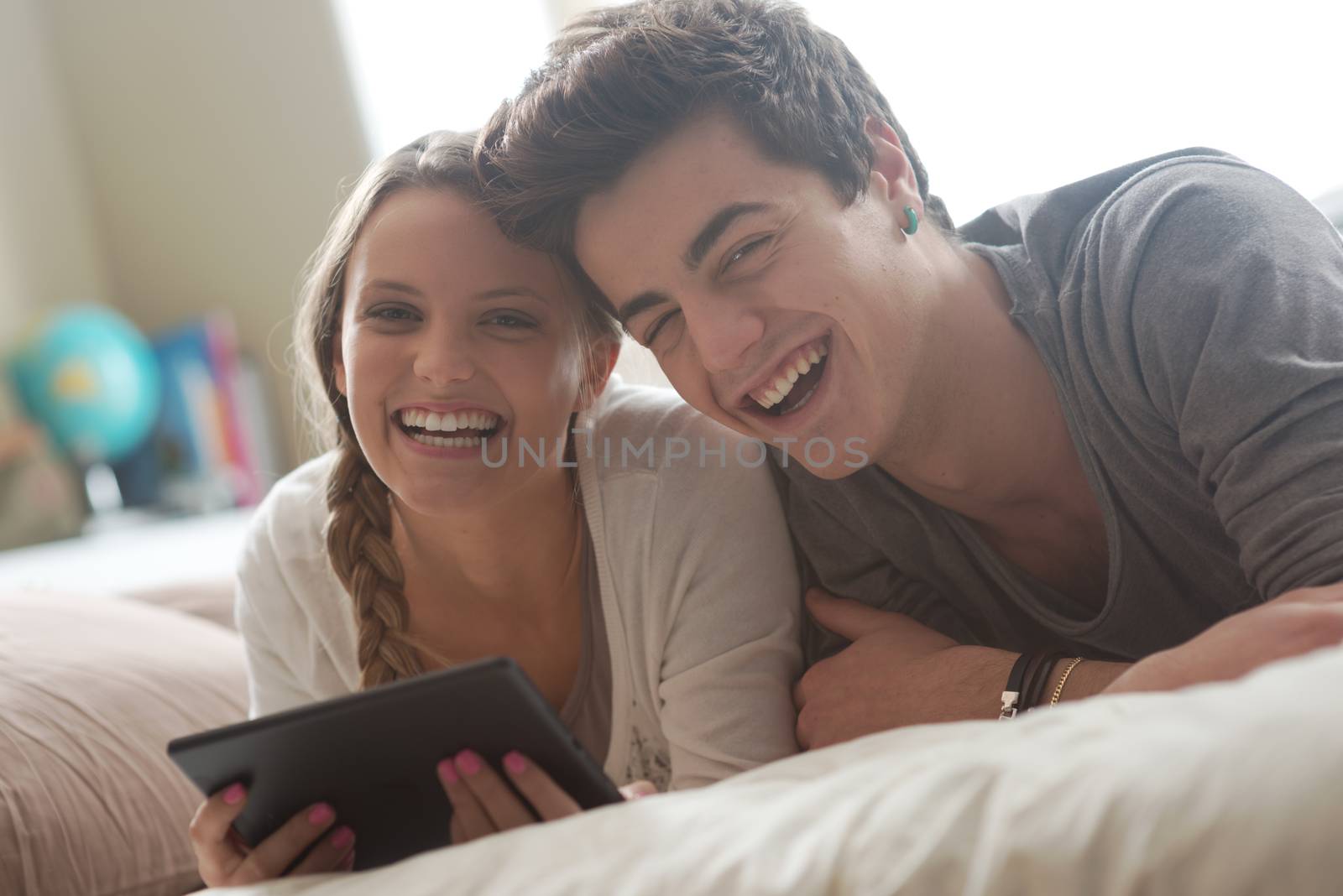 Happy young couple lying on the bed in a bedroom and using digital tablet.